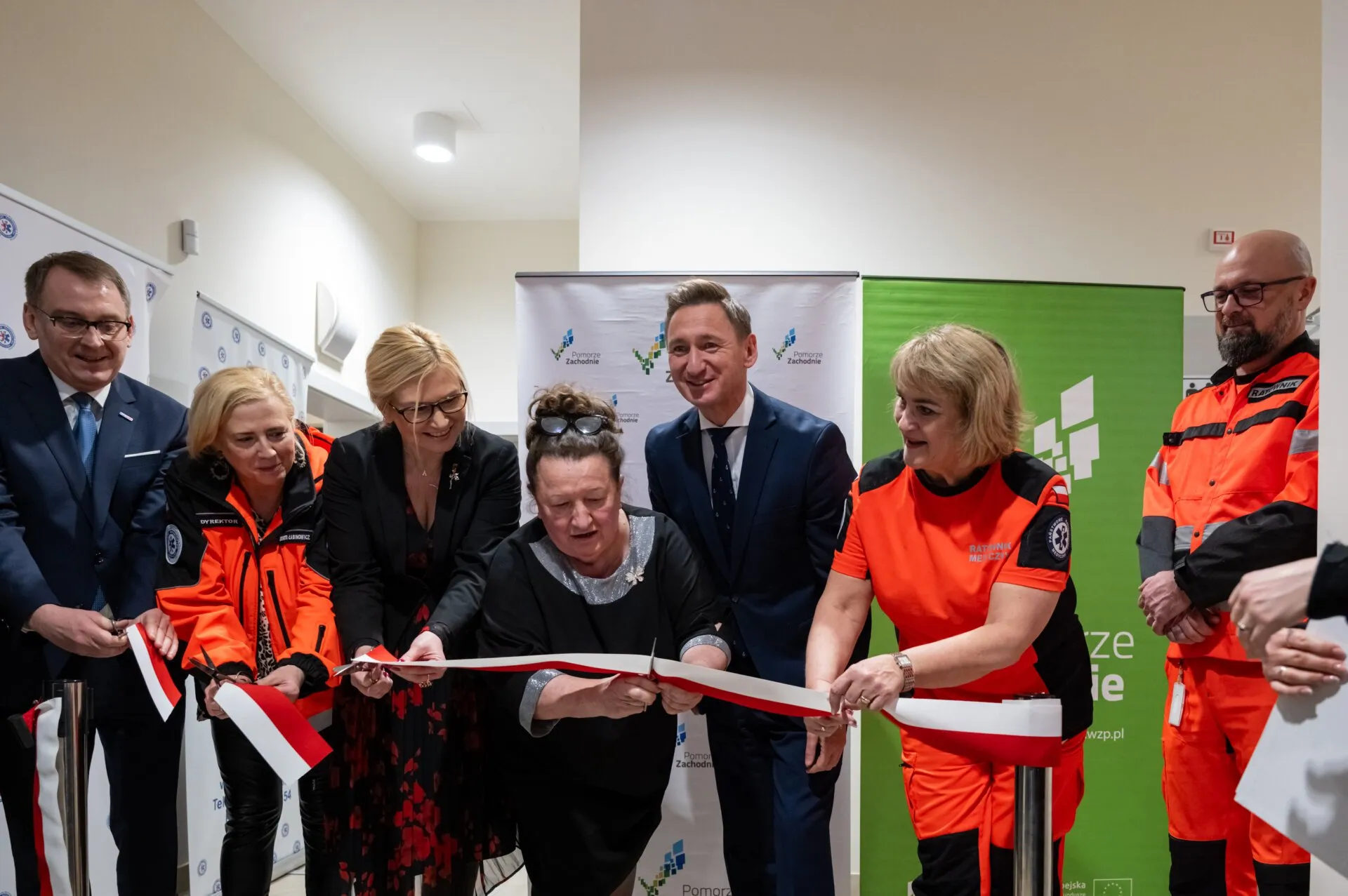 Goście otwarcia filii WSPR w Drawsku Pomorskim przecinają wstęgę, w tle korytarz i ścianki promocyjne.