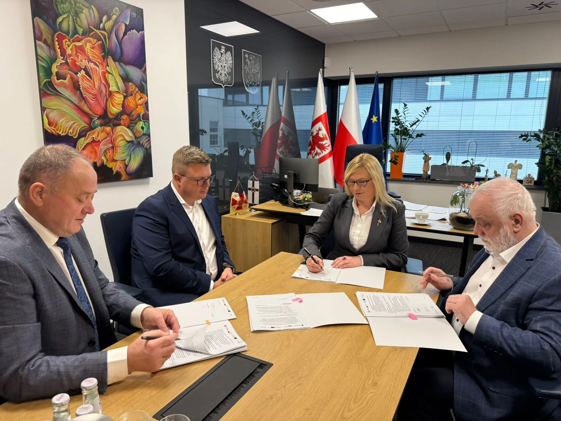 Strony porozumienia podpisują umowę, w tle gabinet wicemarszałkini województwa i flagi.