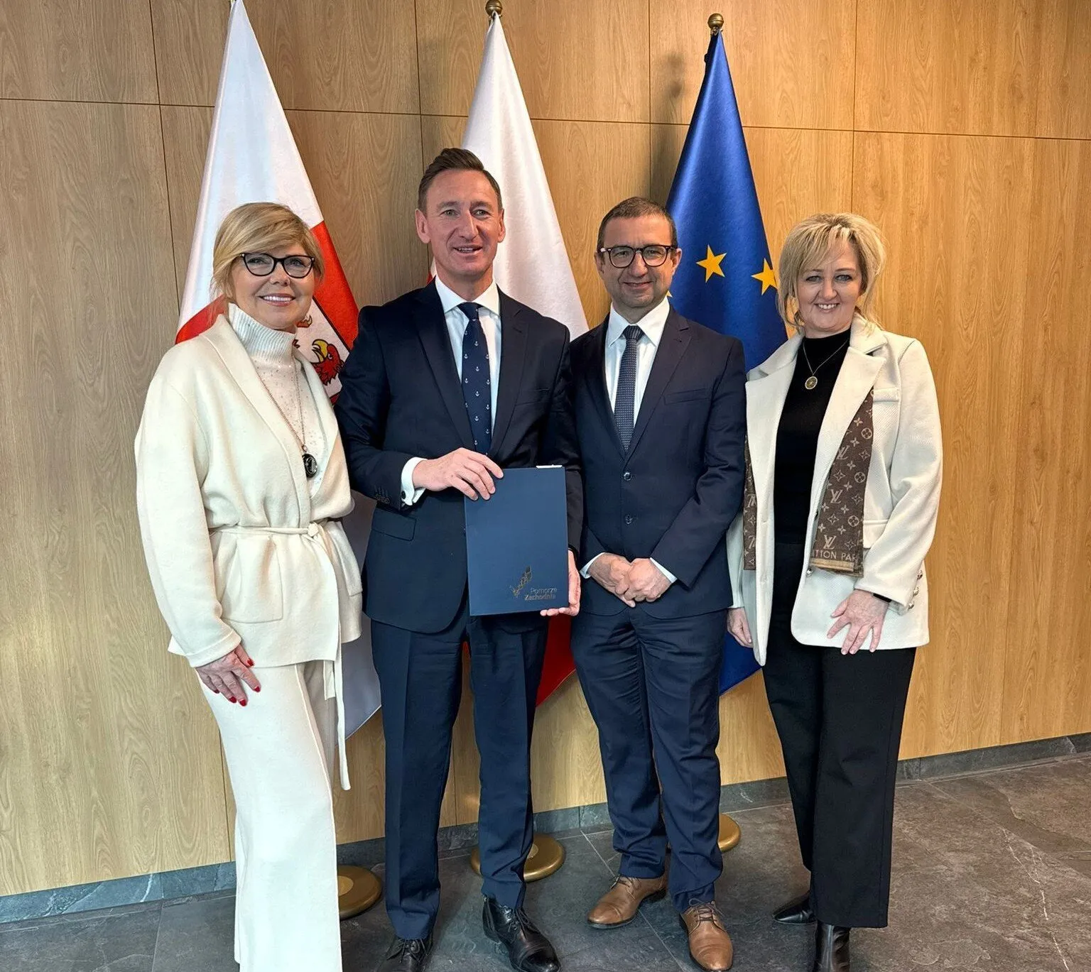 Strony umowy prezentują podpisany dokument, w tle flagi.