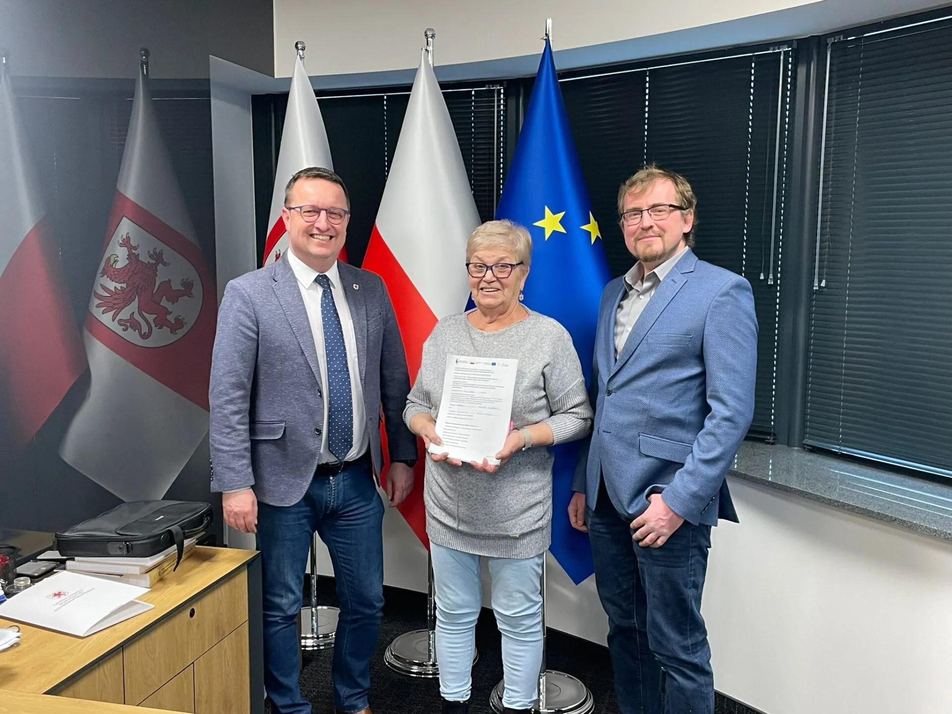 Od lewej Bogdan Jaroszewicz, obok 2 przedstawicieli WM, stoją w gabinecie, kobieta w środku trzyma w dłoni teczkę z umową