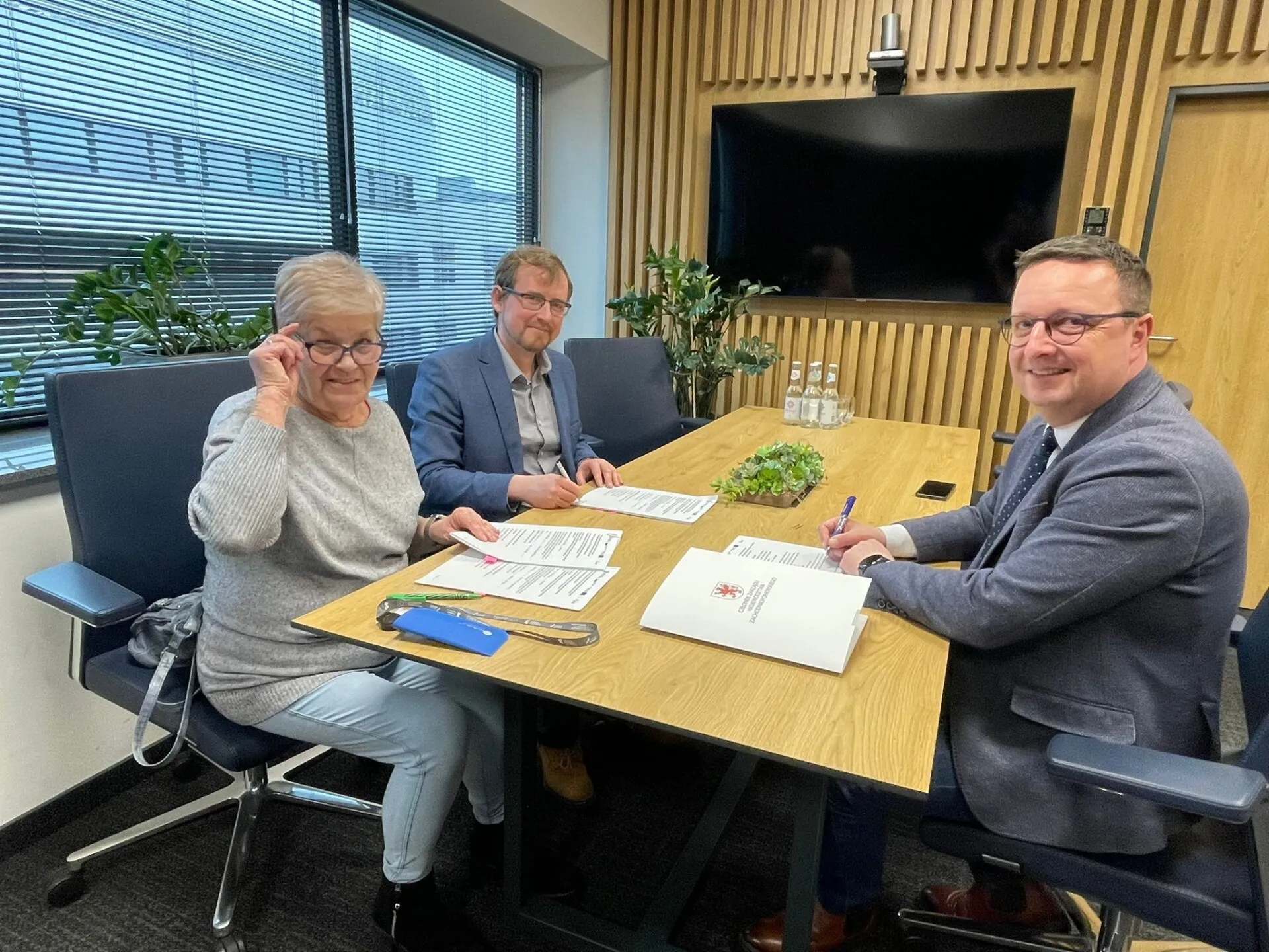 podpisanie umowy dotacyjnej, przy oknie siedzą beneficjenci