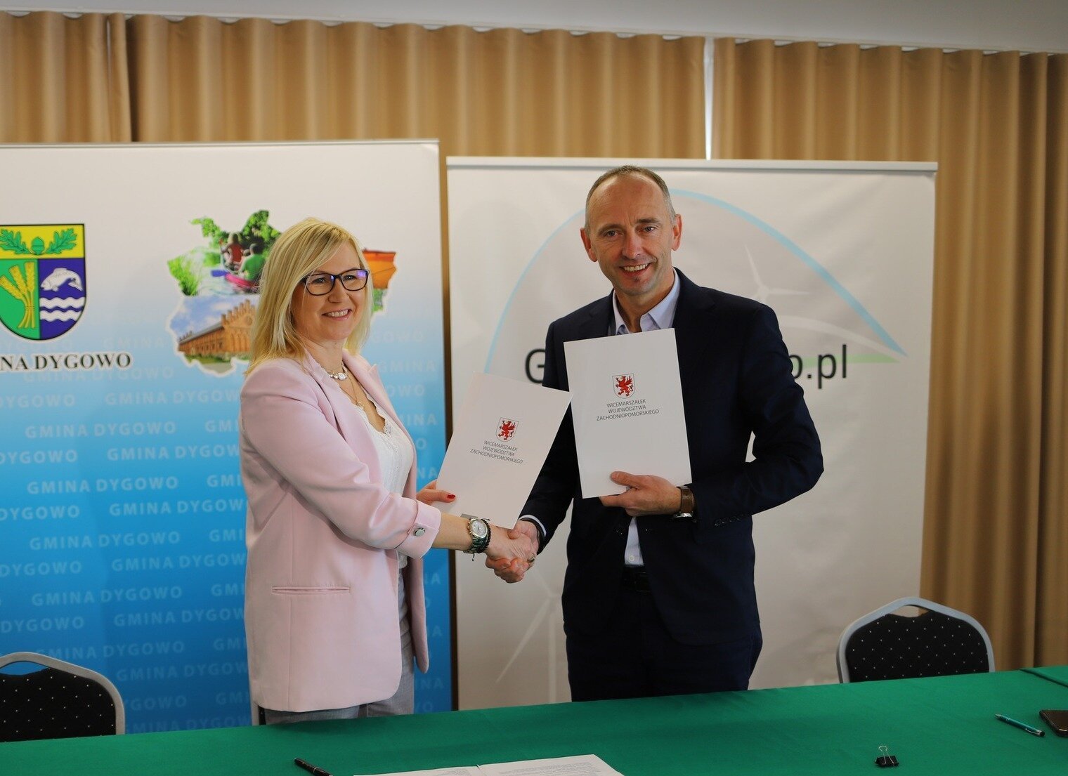 Strony umowy gratulują sobie podpisania porozumienia, w tle ścianki promocyjne.