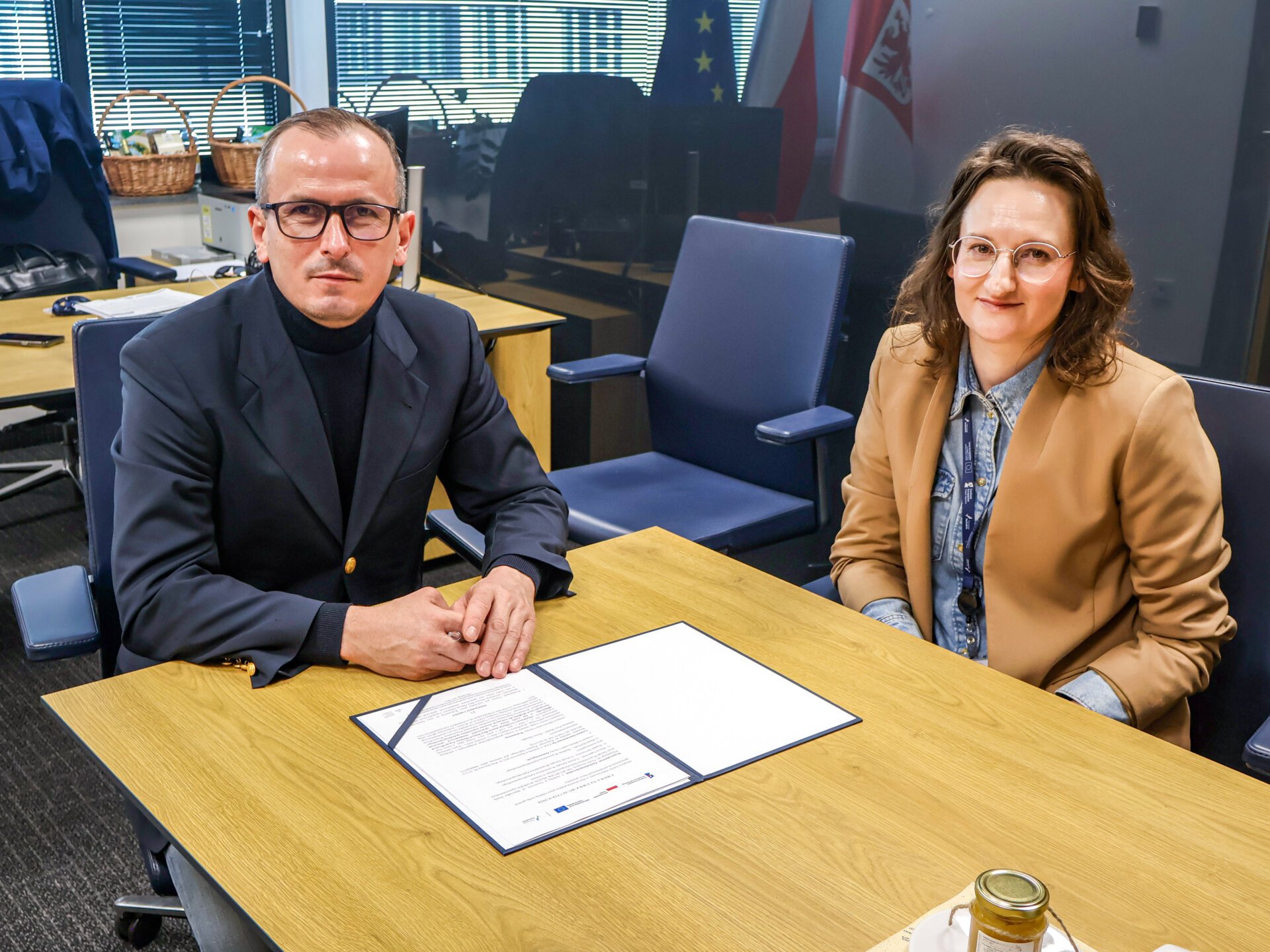 Strony umowy podpisują porozumienie siedząc za stołem prezydialnym, w tle wyposażenie gabinetu członka Zarządu Województwa.