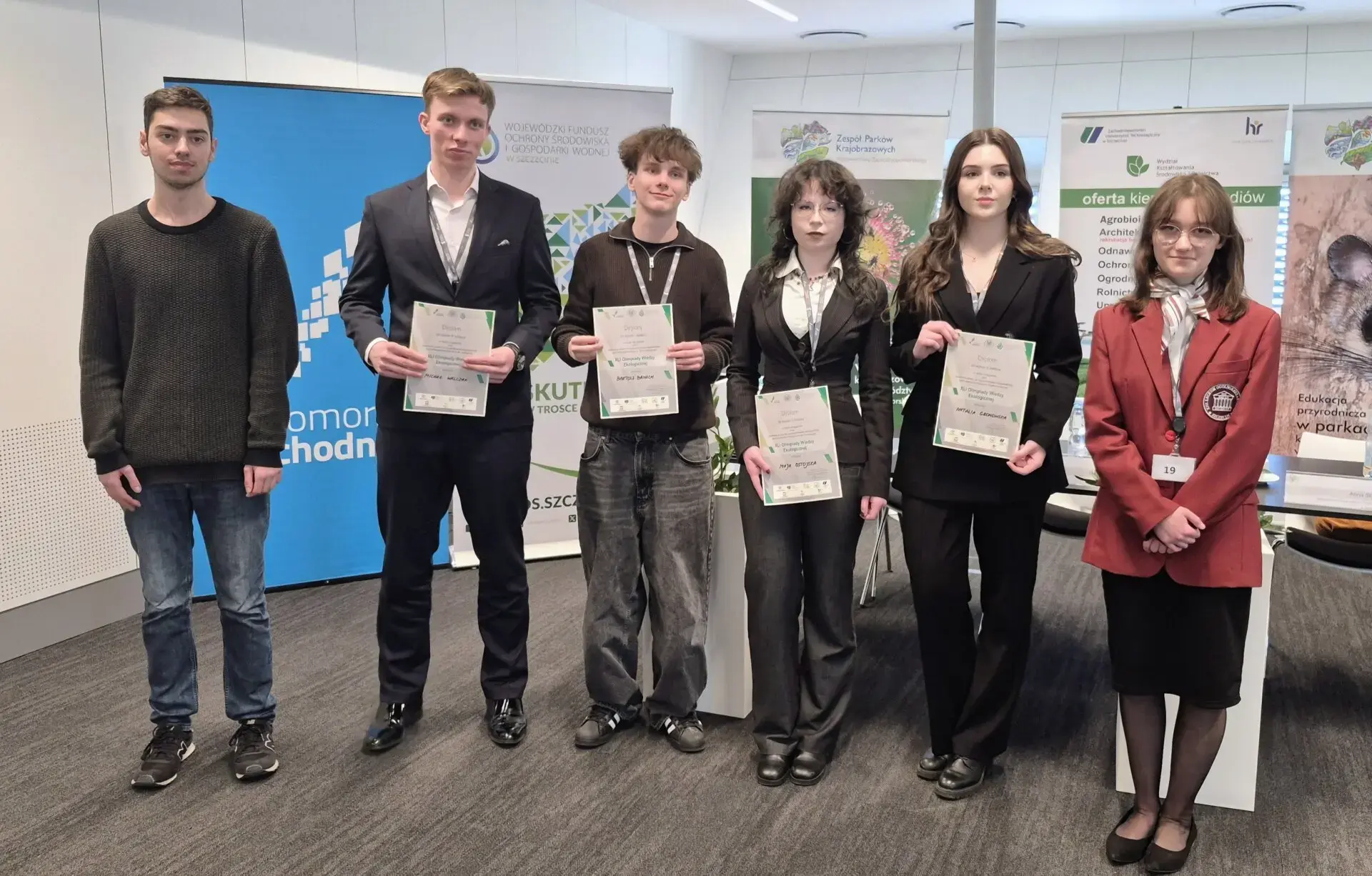 Laureaci etapu regionalnego prezentują pamiątkowe dyplomy, w tle banery promocyjne instytucji organizujących olimpiadę.