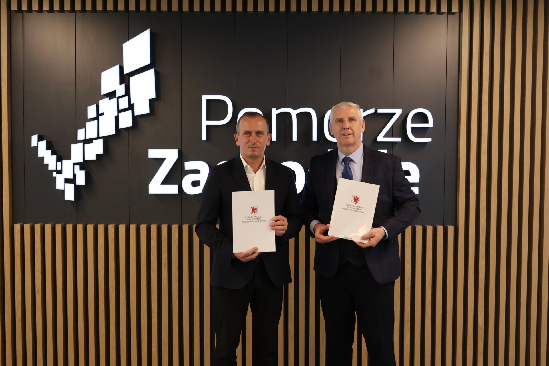 Strony umowy prezentują podpisany dokument, w tle logo z napisem Pomorze Zachodnie.
