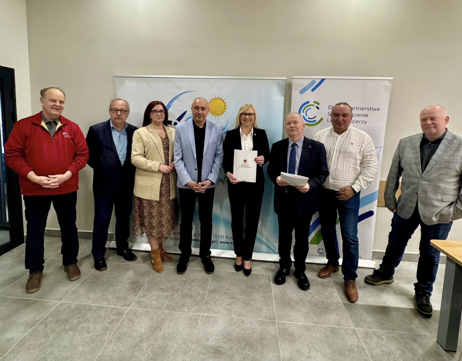 Sygnatariusze umowy oraz zaproszeni goście prezentują podpisane dokumenty, w tle ścianki promocyjne.