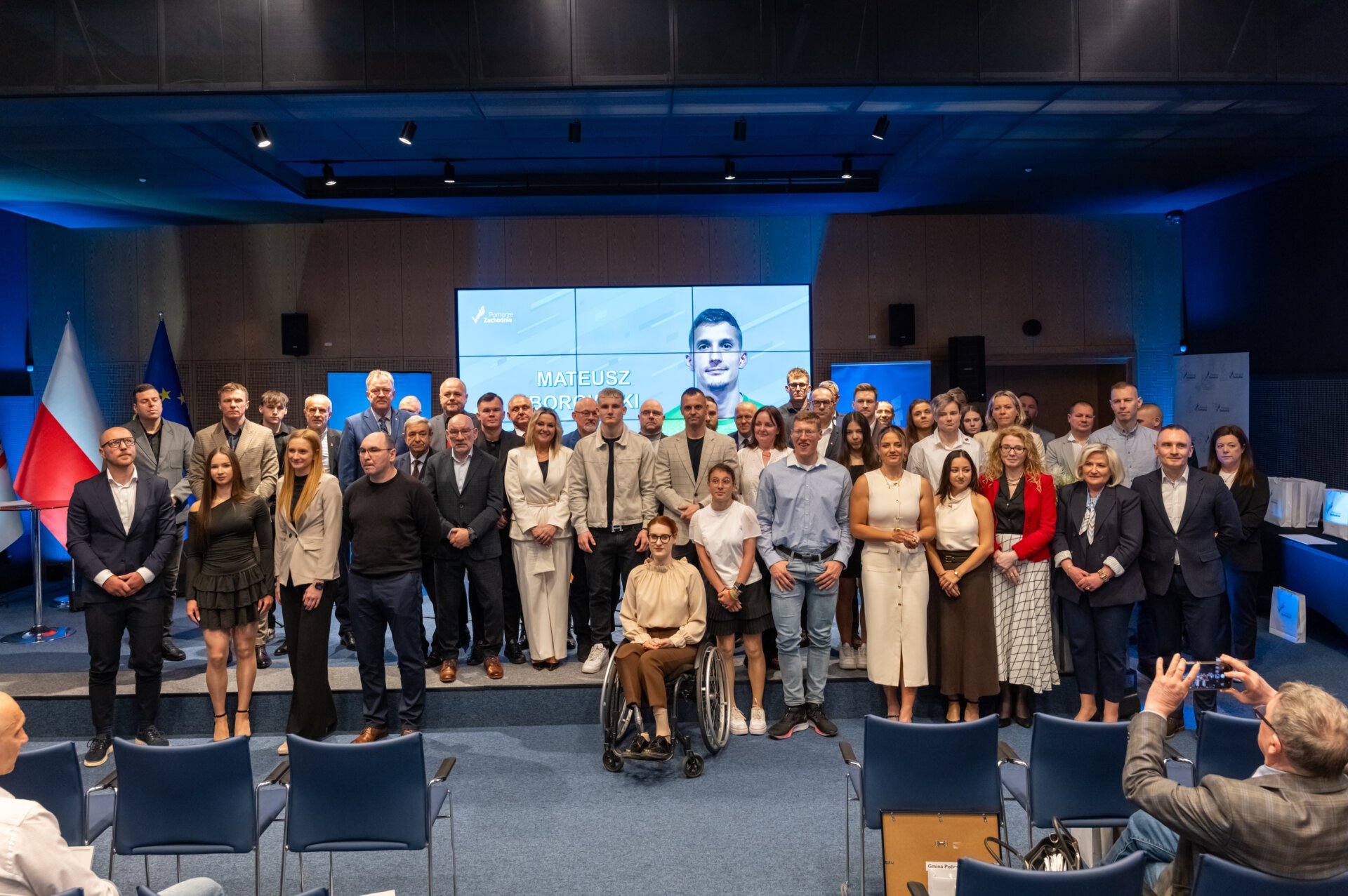 Sportowcy, trenerzy, kluby i samorządowcy na wspólnym zdjęciu, w tle slajd dedykowany gali.