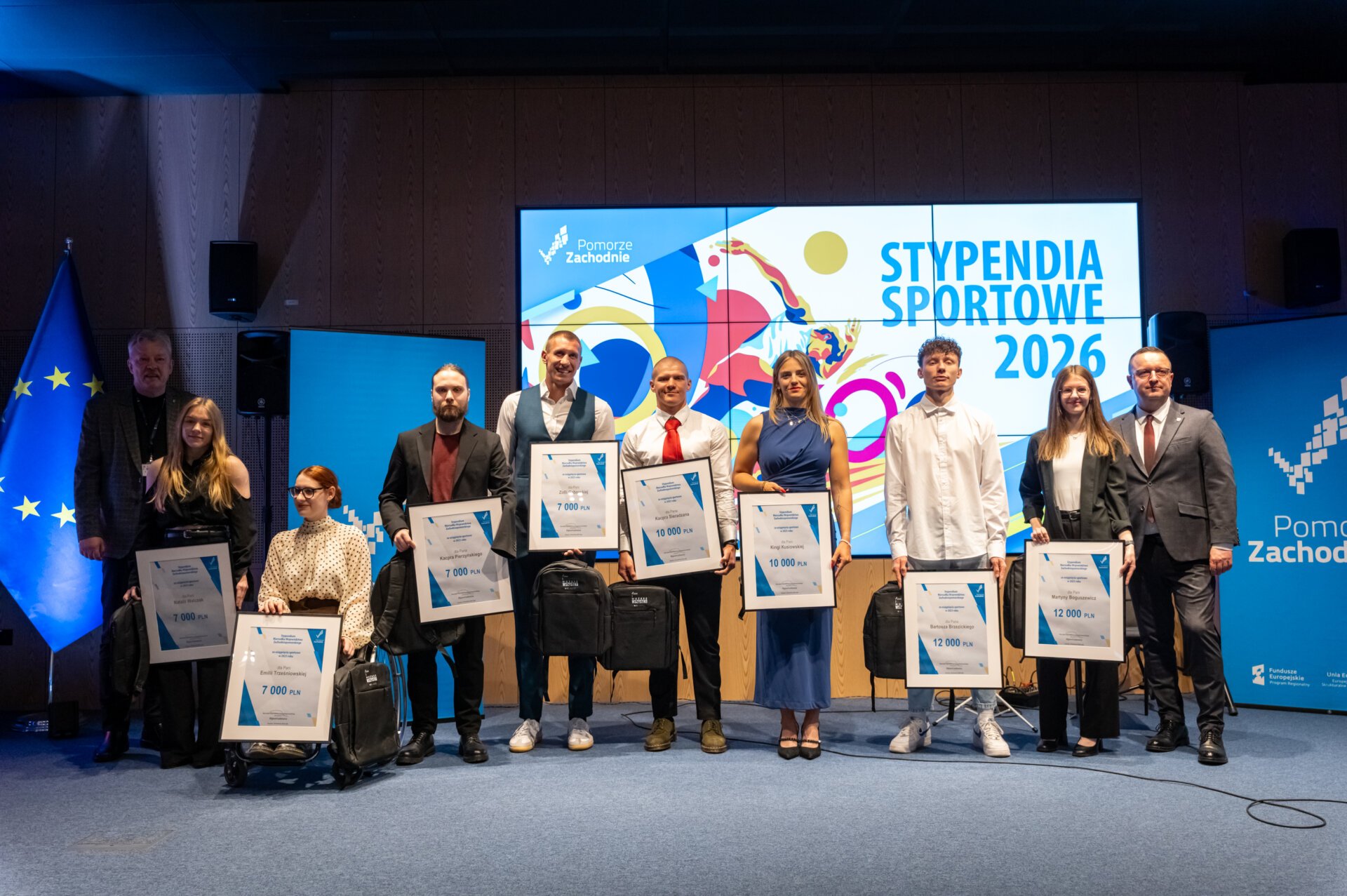 Stypendystki i stypendyści sportowi na scenie z czekami, w tle ekran z napisem Stypendia Sportowe 2026.