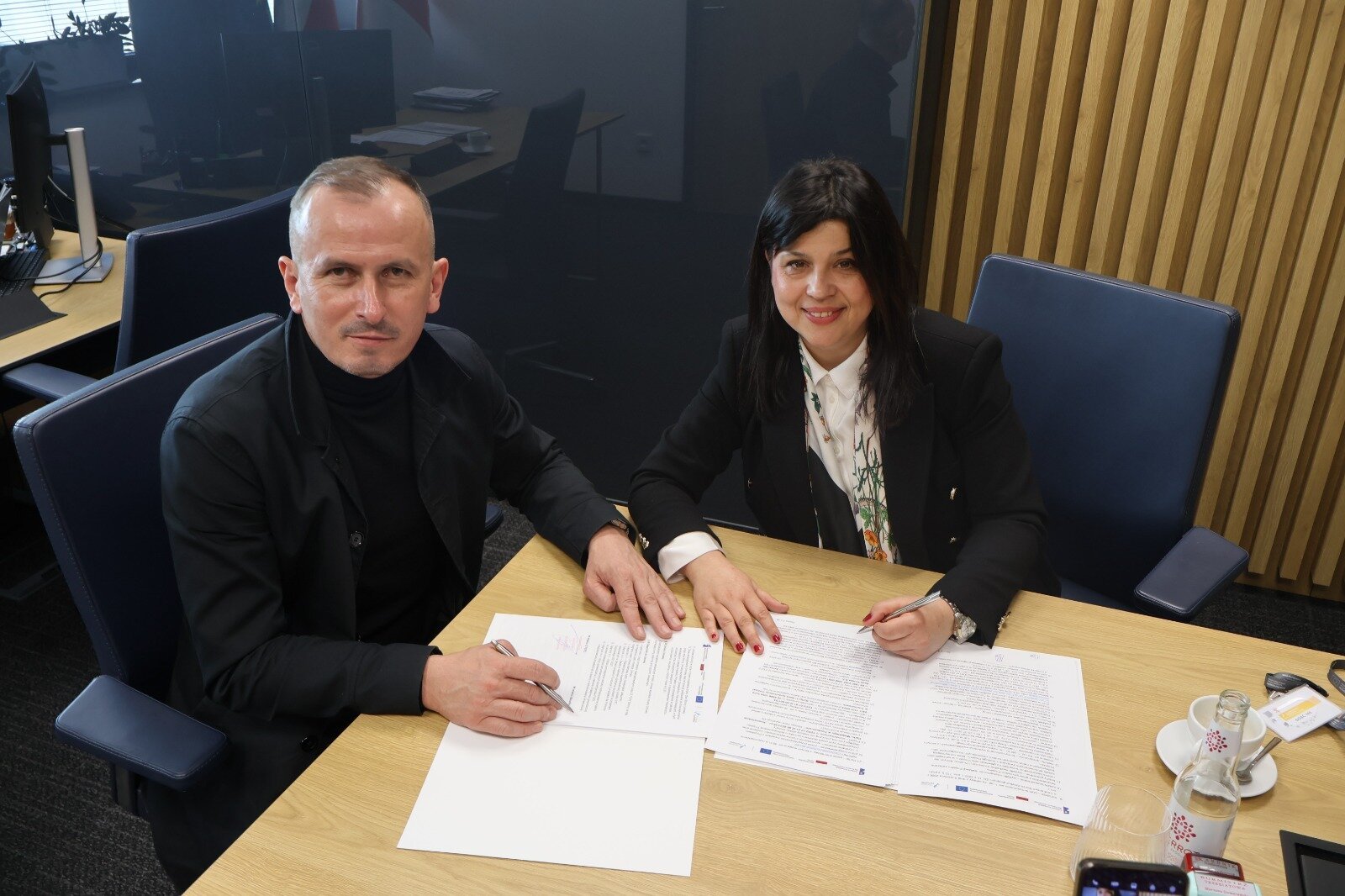 Strony umowy podpisują dokumenty przy stole prezydialnym.