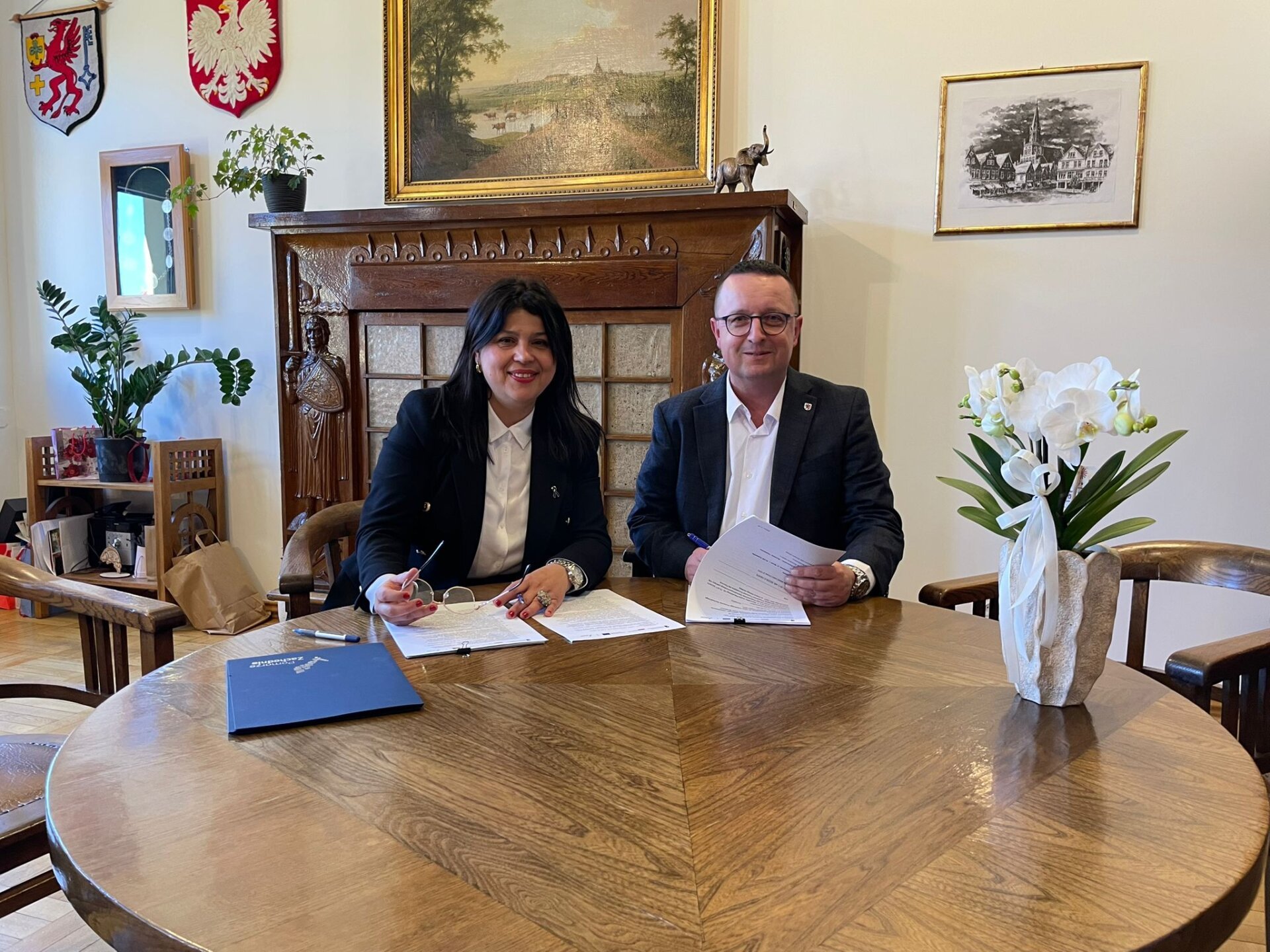 Strony umowy podpisują dokument przy stole prezydialnym, w tle gabinet burmistrzyni Trzebiatowa.