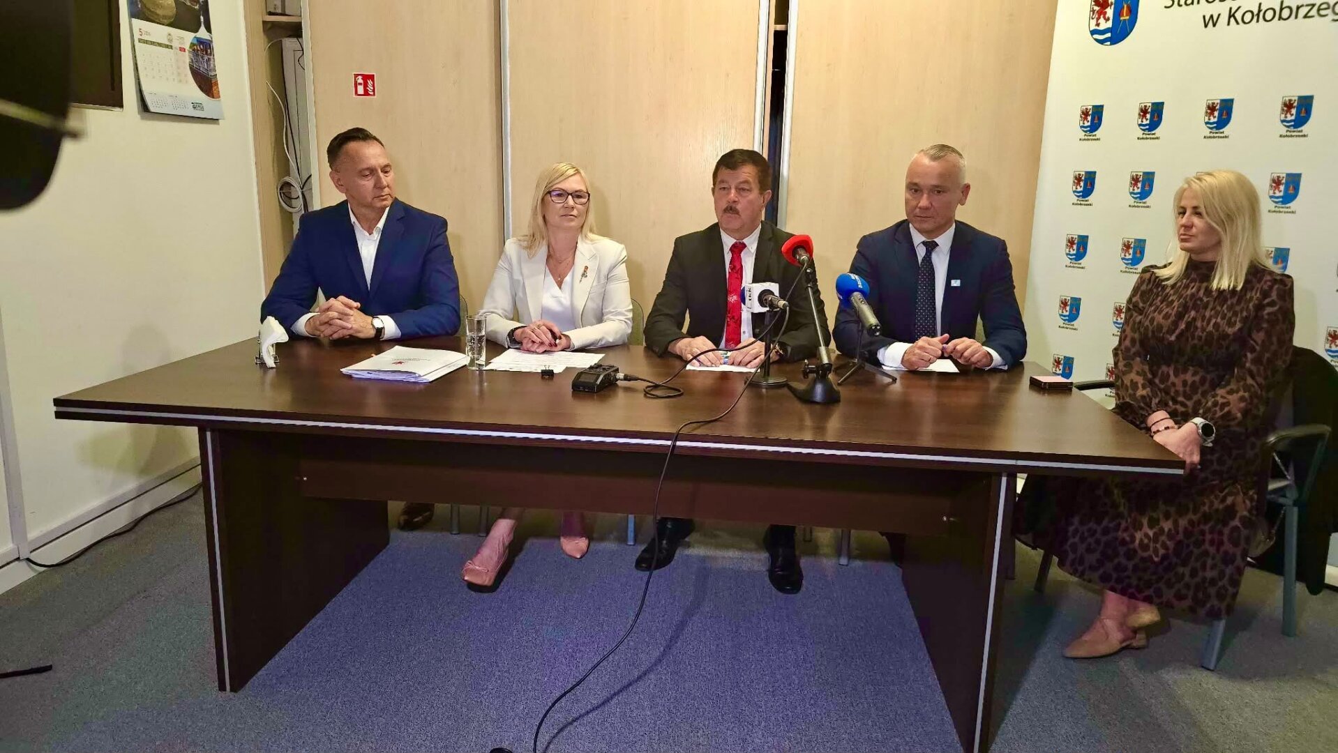 Sygnatariusze umowy siedzą za stołem prezydialnym i mówią o inwestycji.