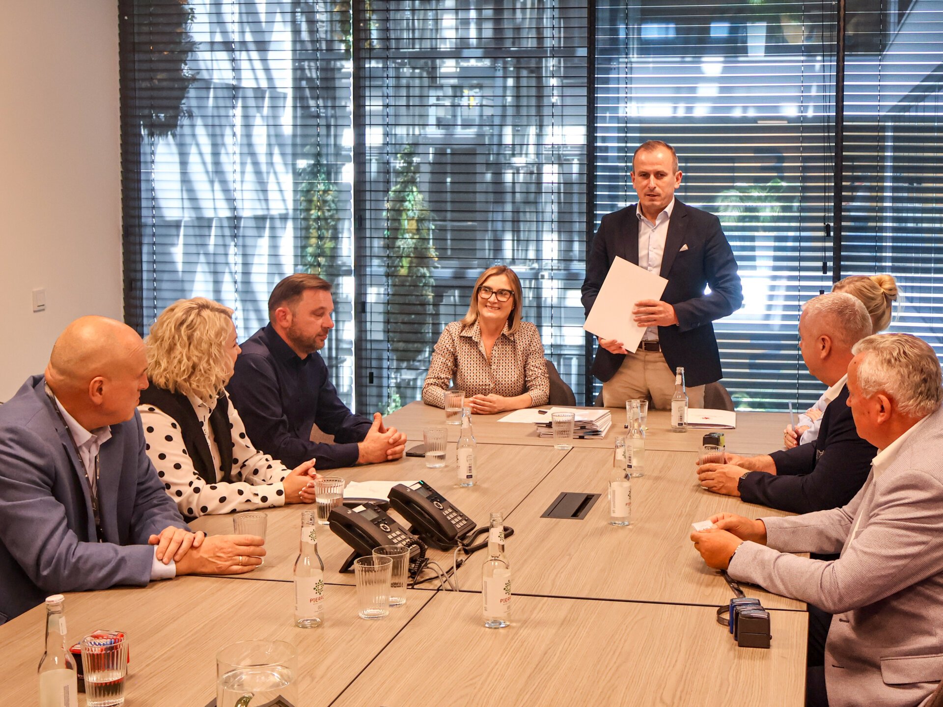 Uczestnicy podpisania umowy siedzą przy stole prezydialnym, przed nimi stoi marszałek Łapeciński i przemawia.