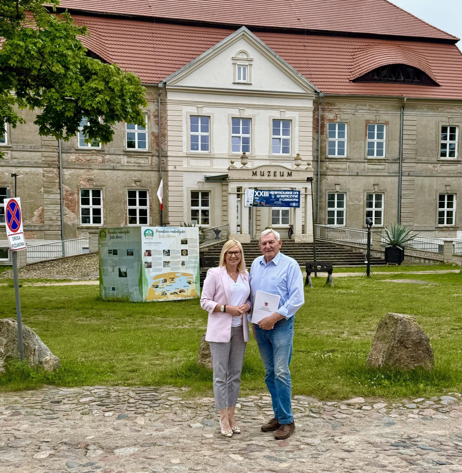 Strony umowy prezentują podpisany dokument, w tle pałac w Siemczynie.