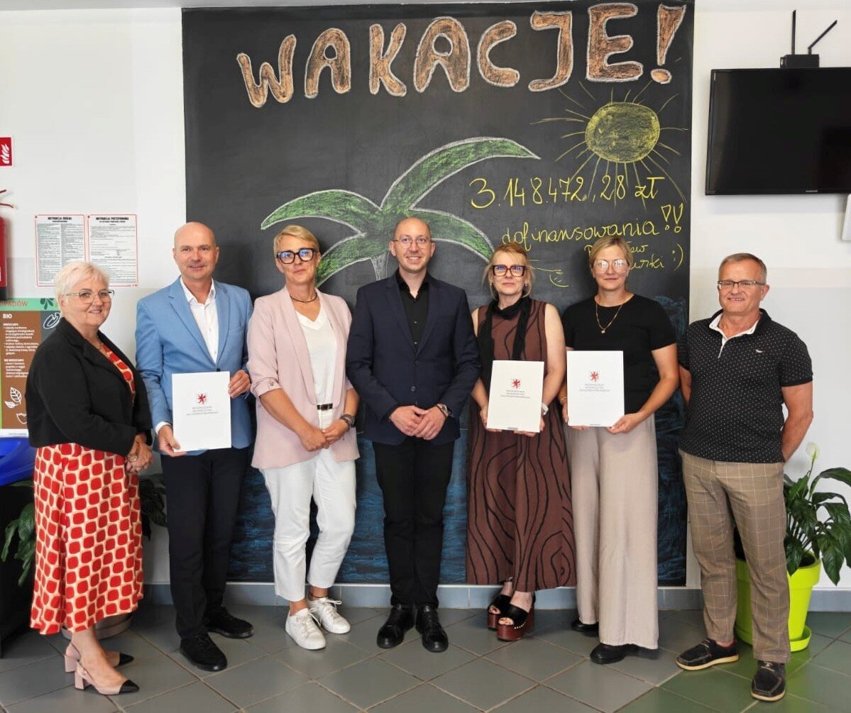 wspólne zdjęcie uczestników spotkania, w tle napis na czarnej tablicy WAKACJE