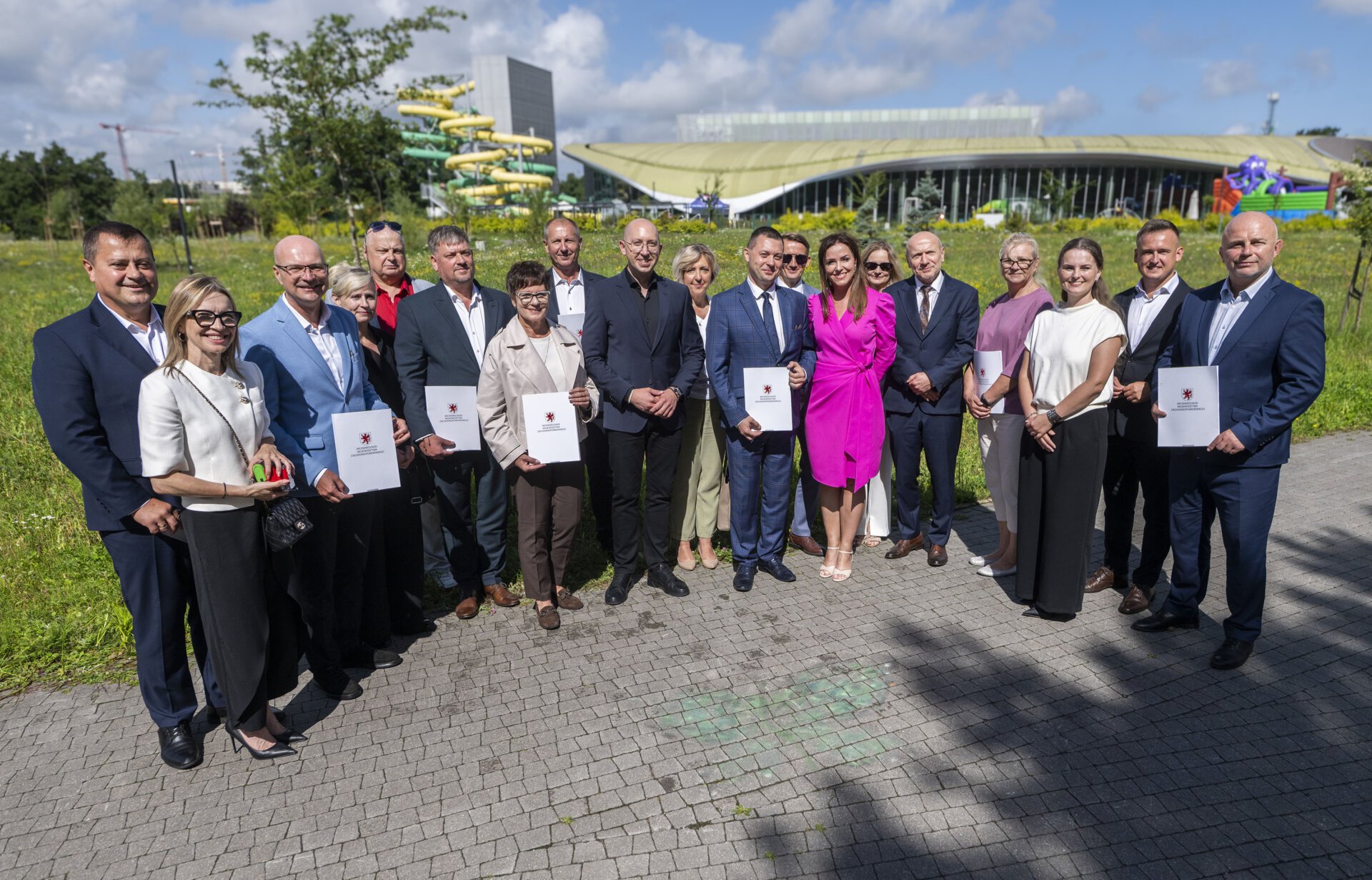 Sygnatariusze umów prezentują podpisane dokumenty, w tle Park Wodny Koszalin.