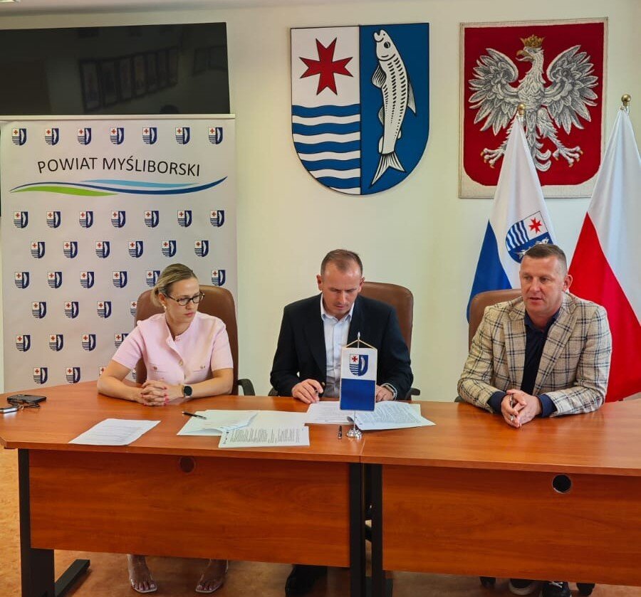 Strony umowy podpisują porozumienie za stołem prezydialnym, w tle ścianka starostwo w Myśliborzu i flagi, herb i godło państwowe.