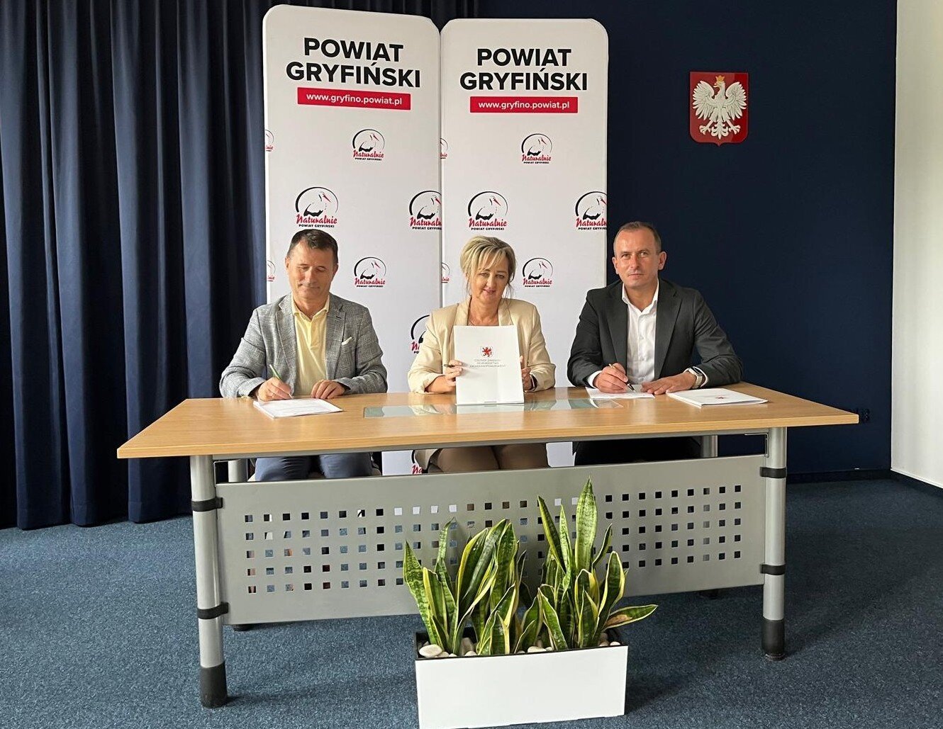 Strony podpisują umowę przy stole prezydialnym, w tle ścianka z napisem Powiat Gryfiński.