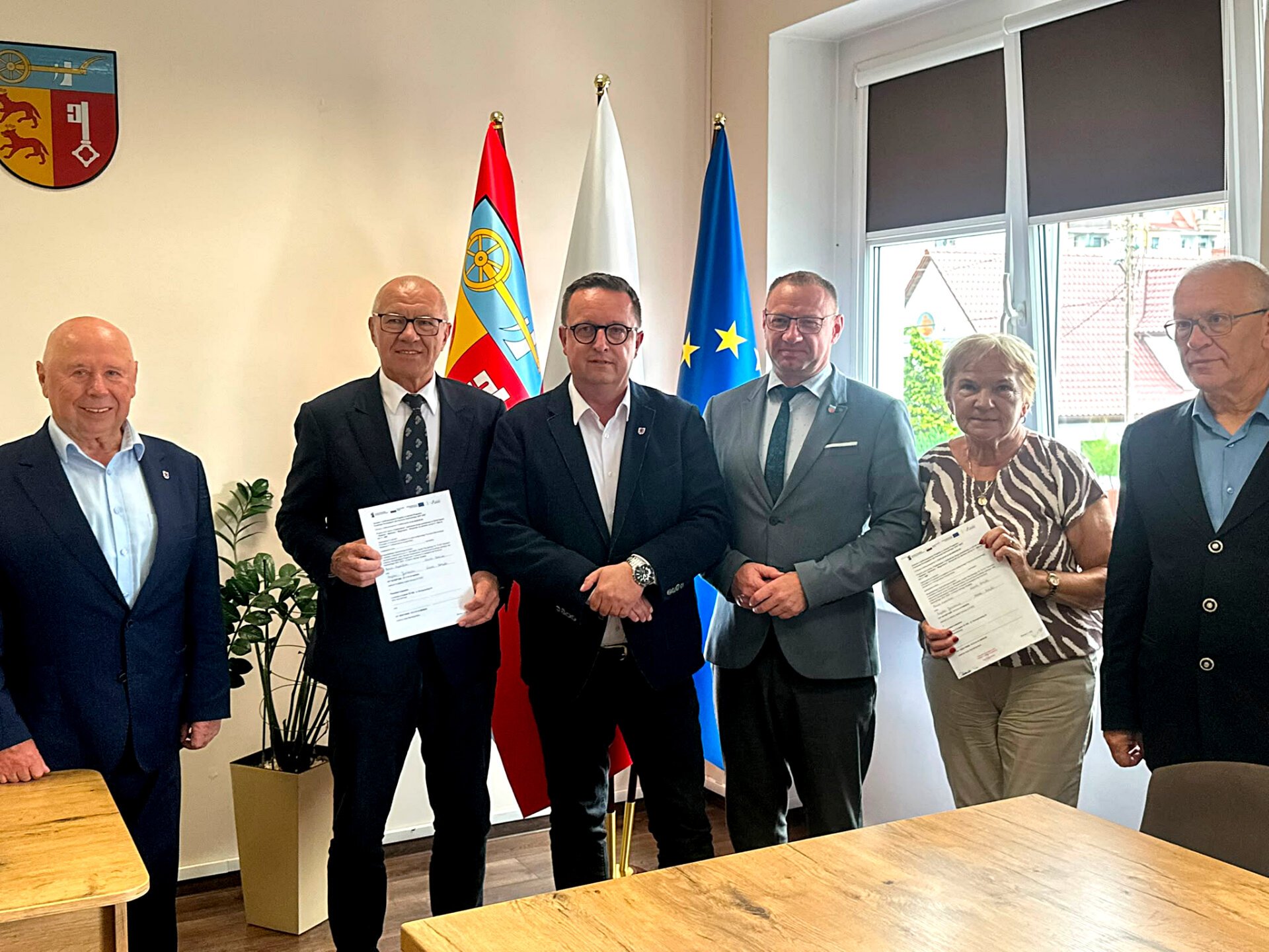 Strony porozumienia prezentują podpisaną umowę, w tle flagi.