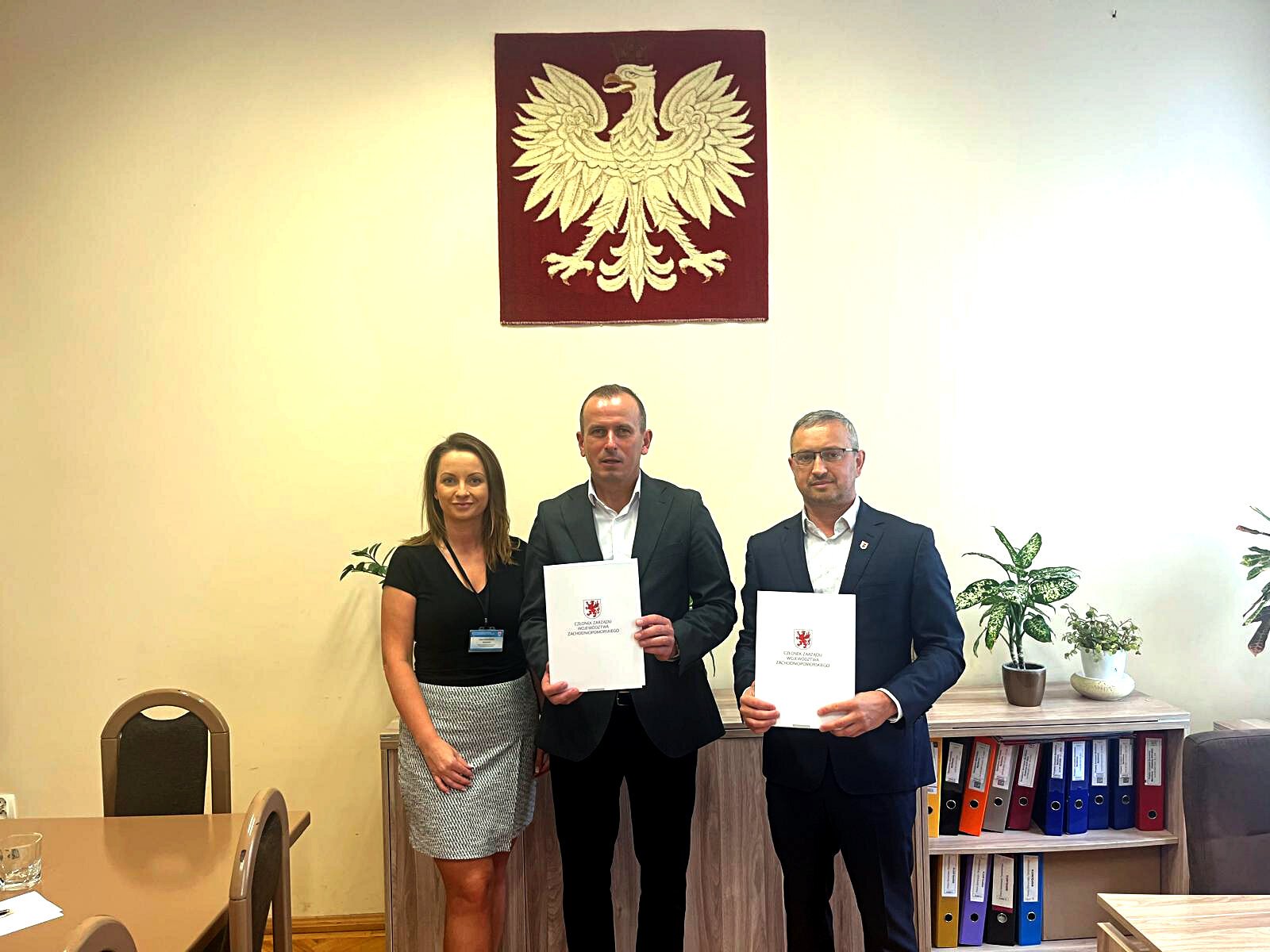 Strony prezentują podpisaną umowę, w tle godło Polski.