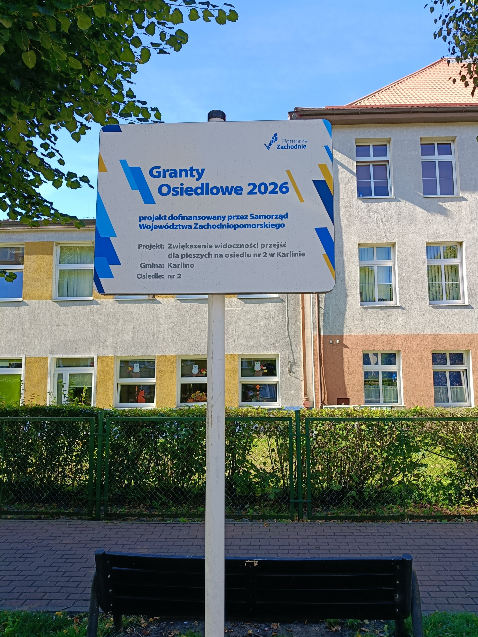 tablica informacyjna o dofinansowaniu zadania z grantu osiedlowego 2026. tablica biała napisy niebiesko, szaro, żółte