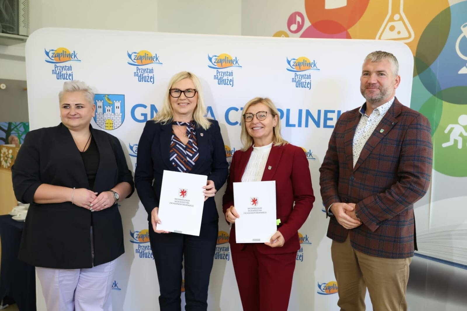 Strony umowy prezentują podpisane porozumienie, w tle ścianka promocyjna gminy.